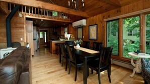 A wooden cabin interior with a dining area, kitchen, and a large window offering a view of the outdoors. - Private Lakeside near Burlington, Oversized Dock Skiing, Shopping, Fine Dining (Colchester)