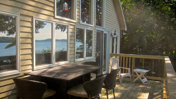 A deck with a table and chairs, overlooking a body of water. - Private Lakeside near Burlington, Oversized Dock Skiing, Shopping, Fine Dining (Colchester)