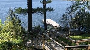 A wooden deck with a metal railing leading to a dock over a lake, surrounded by trees and greenery. - Private Lakeside near Burlington, Oversized Dock Skiing, Shopping, Fine Dining (Colchester)