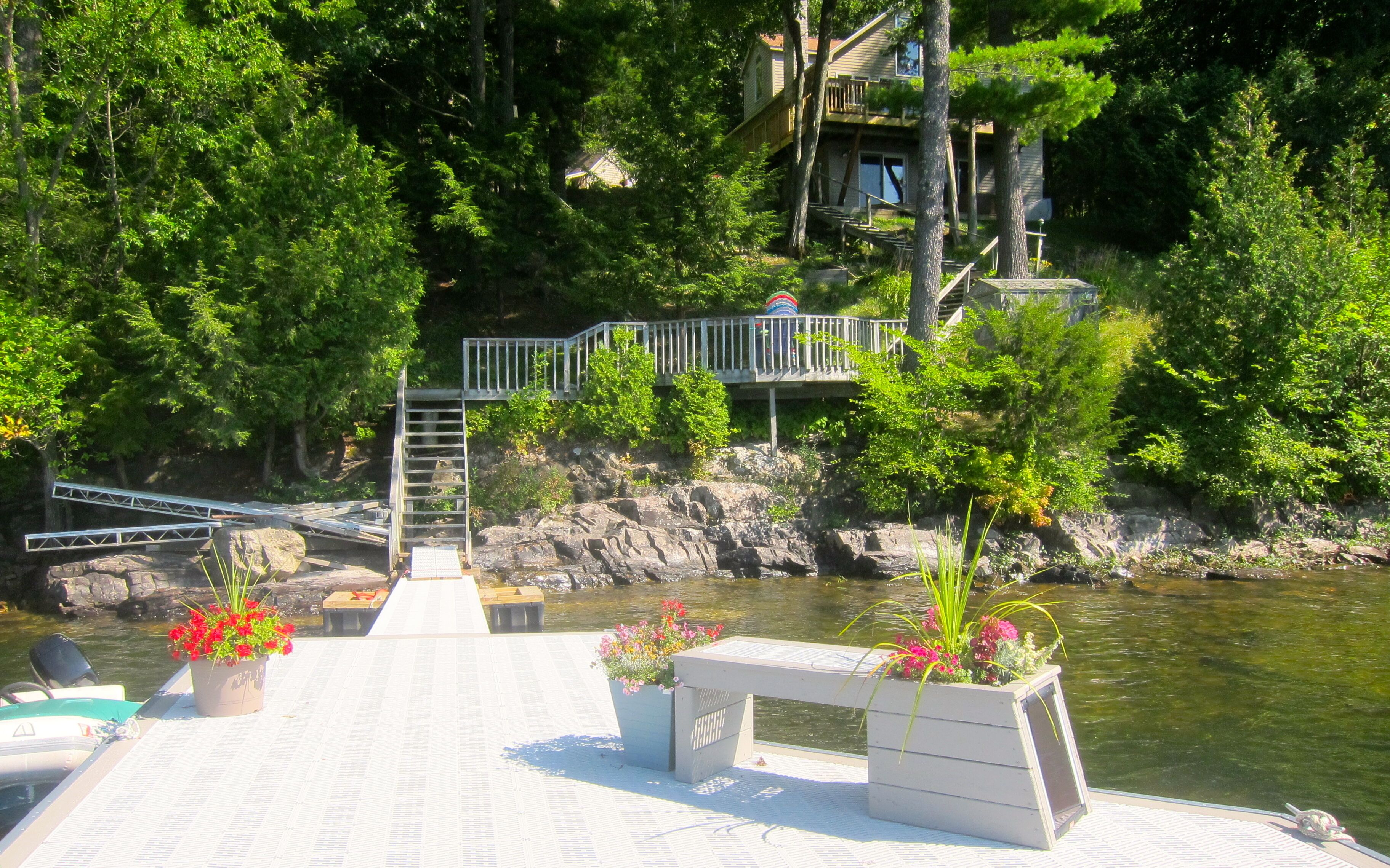 A dock with a wooden walkway leading to a bridge, surrounded by lush greenery and a calm body of water.