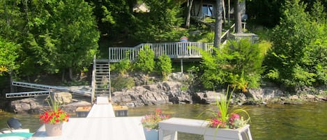 A dock with a wooden walkway leading to a bridge, surrounded by lush greenery and a calm body of water.