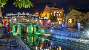 Un puente tradicional con barandillas ornamentales, un camino de piedra y una vía fluvial tranquila que refleja el puente.