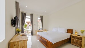 Un dormitorio con una cama de madera, una mesita de noche de madera, un televisor montado en la pared y una pequeña mesa con un jarrón de flores.
