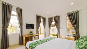 Una habitación de hotel con cama, escritorio, televisión y cortinas.