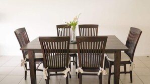 A dining table with four chairs, each with a white ribbon tied around the backrest. A vase with flowers is placed on the table. - Resort Style Apartment-3beds, 2bath, 3 Pools (West End)