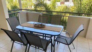 A balcony with a glass table and four chairs, a woven placemat, and a tray with a cup and saucer. - Resort Style Apartment-3beds, 2bath, 3 Pools (West End)