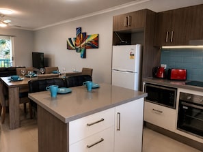 Een moderne keuken met een centraal eiland, witte kasten en een eethoek met een tafel en stoelen.