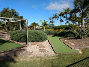Un parcours de minigolf comprenant un green d’entraînement, des bunkers de sable et un pont en bois.