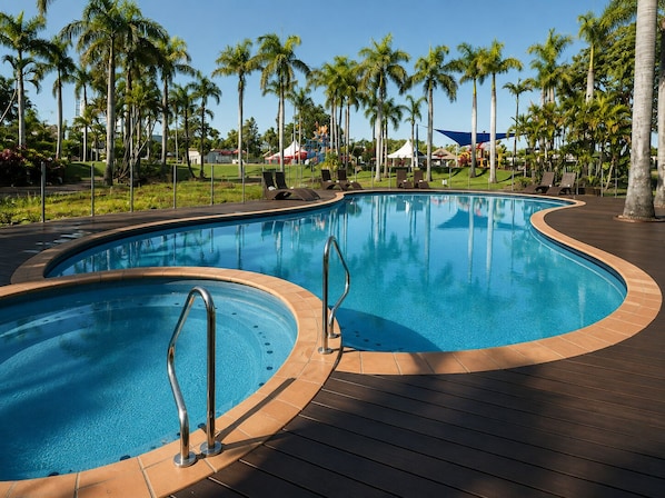 A curved swimming pool with metal railings, surrounded by palm trees and lounge chairs.