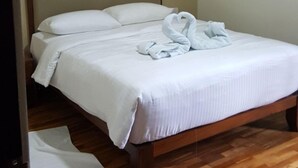 Een net opgemaakt bed met witte lakens en een handdoek in de vorm van een hart.