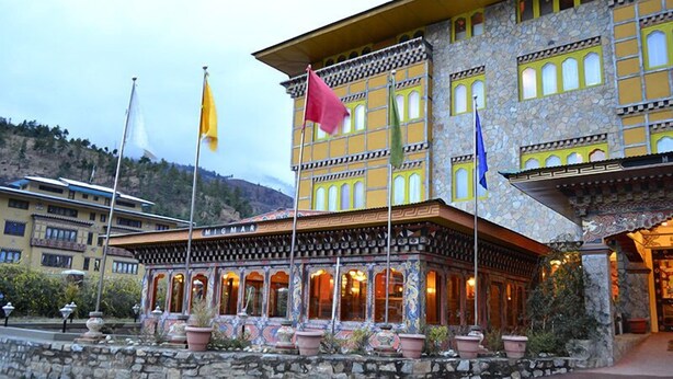 A building with a stone facade and multiple windows, featuring a prominent 'M' sign on the roof. - Hotel Migmar (Thimphu)