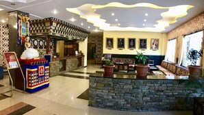 A lobby with a reception desk, a seating area with patterned cushions, and a wall with framed portraits. - Hotel Migmar (Thimphu)