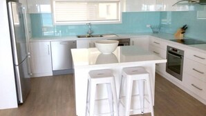 A modern kitchen with white cabinetry, a central island with stools, a window, and a built-in oven. - Millpond - Penneshaw Beach (Penneshaw)