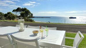 A white table with a pitcher, a bowl, and two drinks with straws, set against a scenic view of the ocean and a distant ship. - Millpond - Penneshaw Beach (Penneshaw)