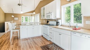 Une cuisine spacieuse avec des meubles blancs, un grand îlot central et une vue sur la verdure environnante.
