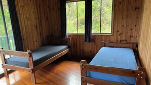 Una cabaña con dos camas de madera, suelo de madera y ventanas grandes con cortinas.