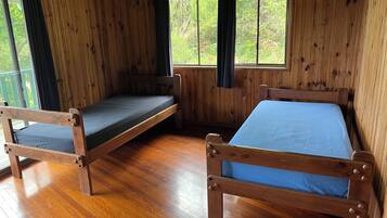 A cabin with two wooden beds, a wooden floor, and large windows with curtains.