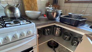 Una cocina con estufa a gas, horno y una despensa empotrada con ollas y sartenes.