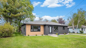 A modern two-story house with a well-maintained lawn and mature trees. - Manistee Channel Waterfront Home with Boat Dock (Manistee)