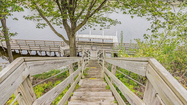 A wooden staircase leading to a dock over water, surrounded by greenery. - Manistee Channel Waterfront Home with Boat Dock (Manistee)