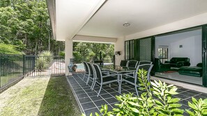 A patio with a glass table and chairs, surrounded by a metal fence and greenery. - Beautiful Gold Coast home, the perfect base for your Commonwealth Games stay (Mudgeeraba)
