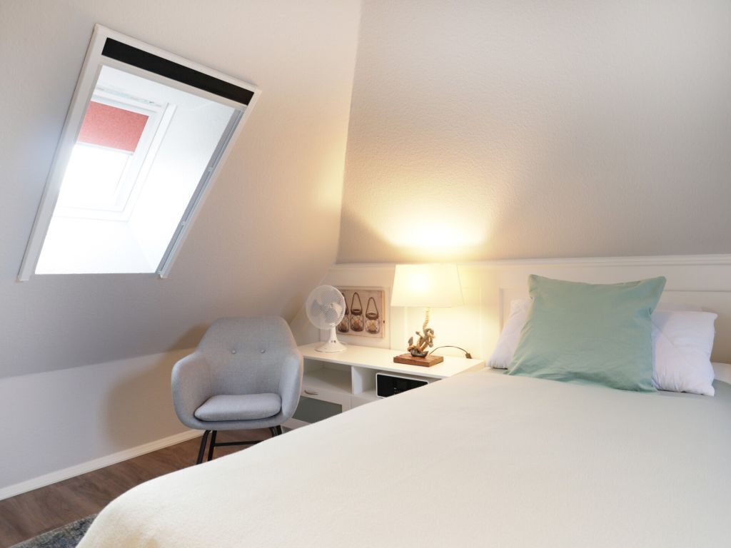 A hotel room with a bed, a desk, a chair, a lamp, and a window.
