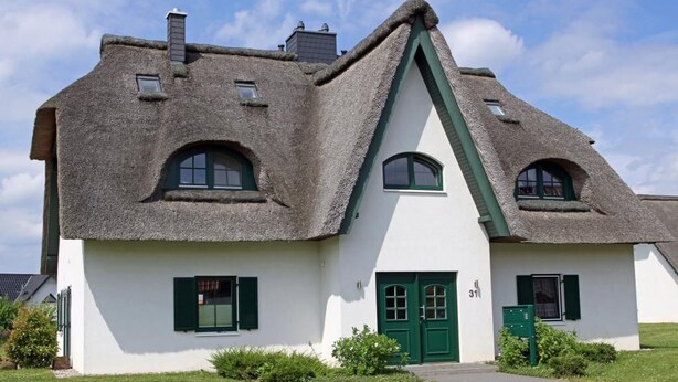 Uma casa tradicional com telhado de palha, fachada branca, persianas verdes e porta verde.