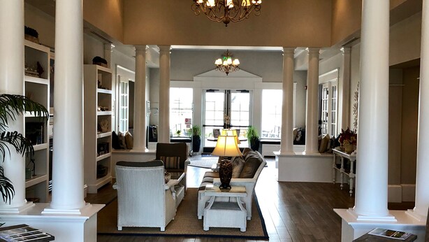 A spacious living room with high ceilings, white columns, and a chandelier. There are sofas, a coffee table, and a rug.