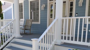 A porch with steps leading to a door, a bench, and a small garden with hydrangea flowers.