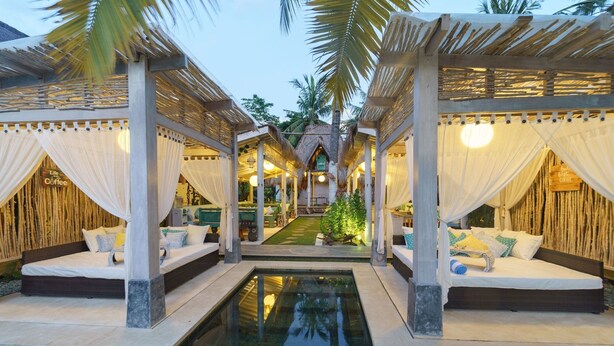 A poolside area with two seating areas, each with a canopy and cushions, connected by a central pathway. - Rascals Boutique Kuta Lombok (Kuta)