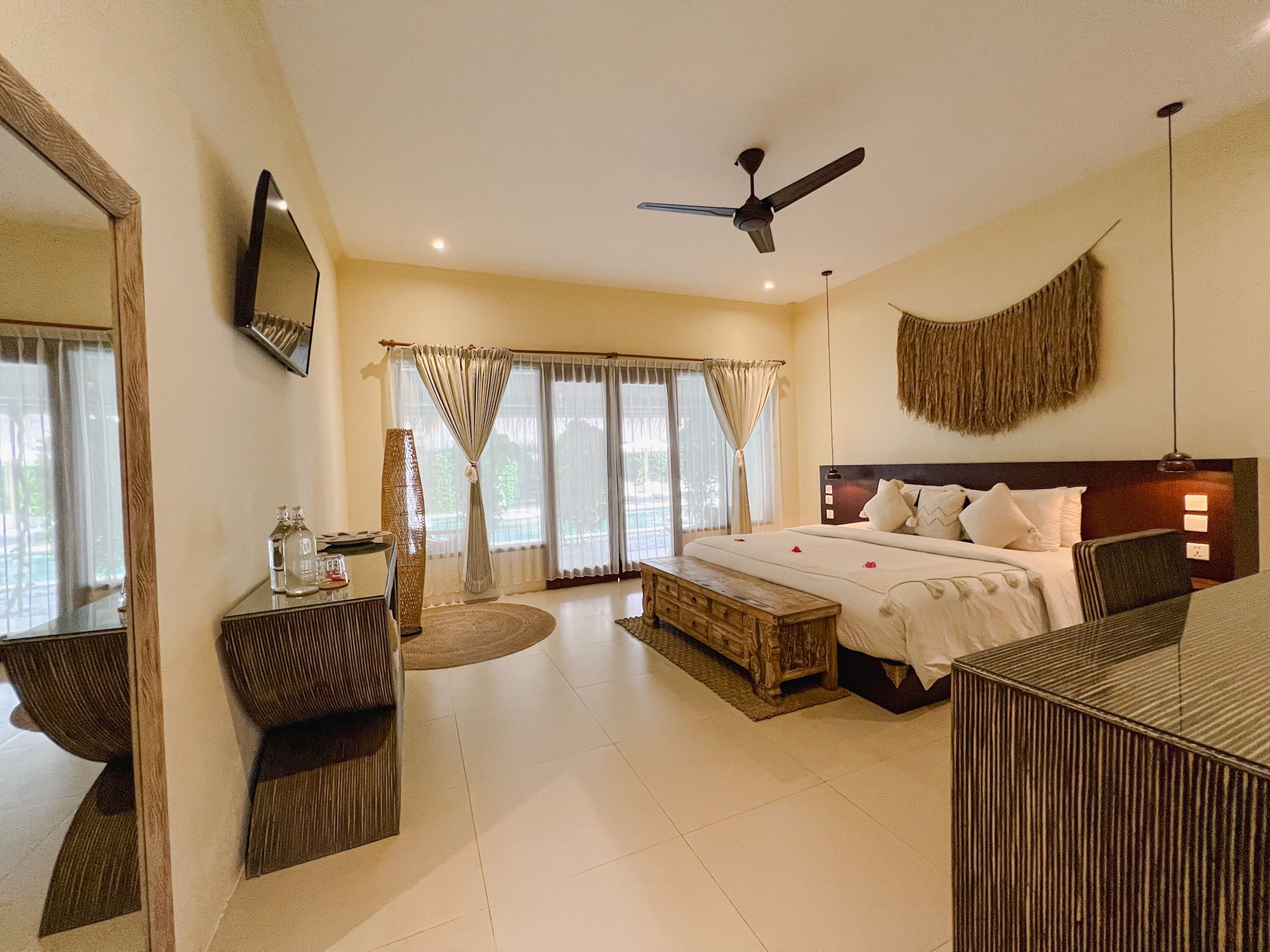 A hotel room with a large bed, a desk, a chair, a ceiling fan, and a large mirror.