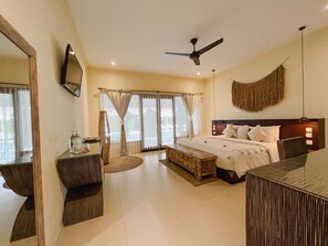 A hotel room with a large bed, a desk, a chair, a ceiling fan, and a large mirror. - Rascals Boutique Kuta Lombok (Kuta)