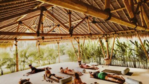 A spacious indoor area with a thatched roof, multiple yoga mats laid out on the floor, and a view of tropical vegetation outside. - Rascals Boutique Kuta Lombok (Kuta)
