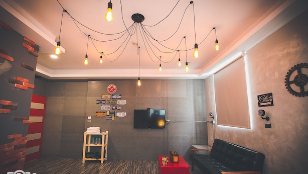 Una habitación moderna con pared de ladrillo decorativa, televisión, mesita auxiliar roja, sofá de cuero negro y una lámpara de techo original.