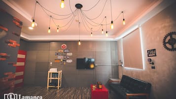 A modern room with a brick accent wall, a television, a red side table, a black leather couch, and a unique ceiling light fixture.