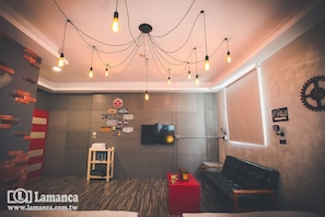 A modern room with a brick accent wall, a television, a red side table, a black leather couch, and a unique ceiling light fixture. - Lamanca B&B (Hualien City)