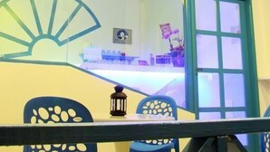 Una habitación con un separador de vidrio, un ventanal con marco azul, una mesa con sillas y una lámpara colgante.