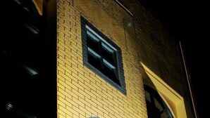 Fachada de edificio iluminada de noche, con detalles arquitectónicos resaltados y un amplio ventanal arqueado.