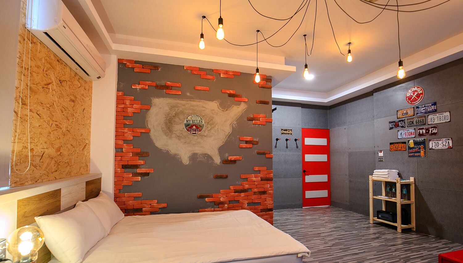 Une chambre avec un lit, une tête de lit en bois, un mur décoré d’une carte, une porte rouge et une étagère avec divers objets.
