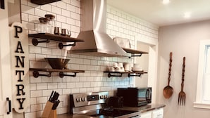 Una cocina con armarios blancos, una estufa de acero inoxidable y un microondas. Hay repisas de madera sobre la estufa y una campana extractora sobre la hornalla.