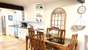 Una cocina con mesa y sillas de madera, armarios blancos y una balanza colgante.