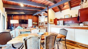 Ein gemütliches Interieur mit einem Holzesstisch, Korbstühlen, einer Küche mit roten Schränken und einem Kamin.