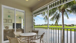 Un balcon avec une table et des chaises, donnant sur un terrain de golf et des palmiers.