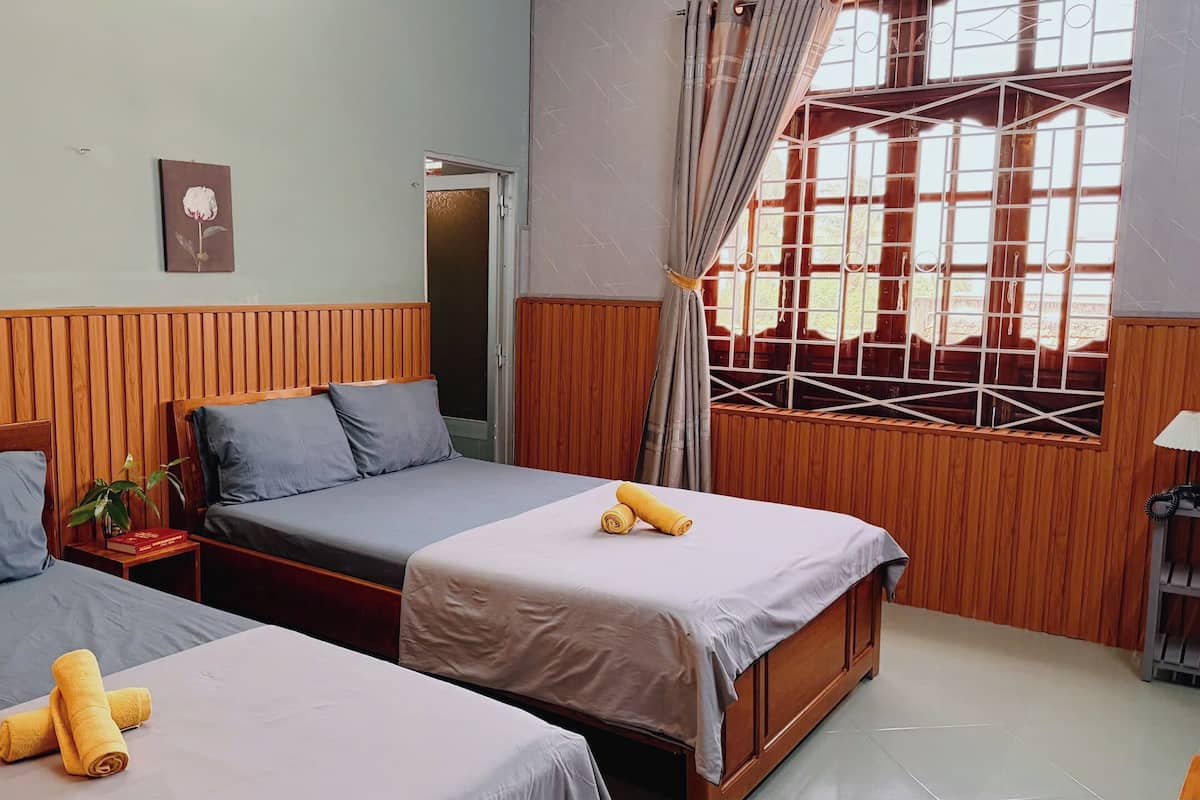 A hotel room with two beds, wooden paneling, a window with metal bars, and a door.