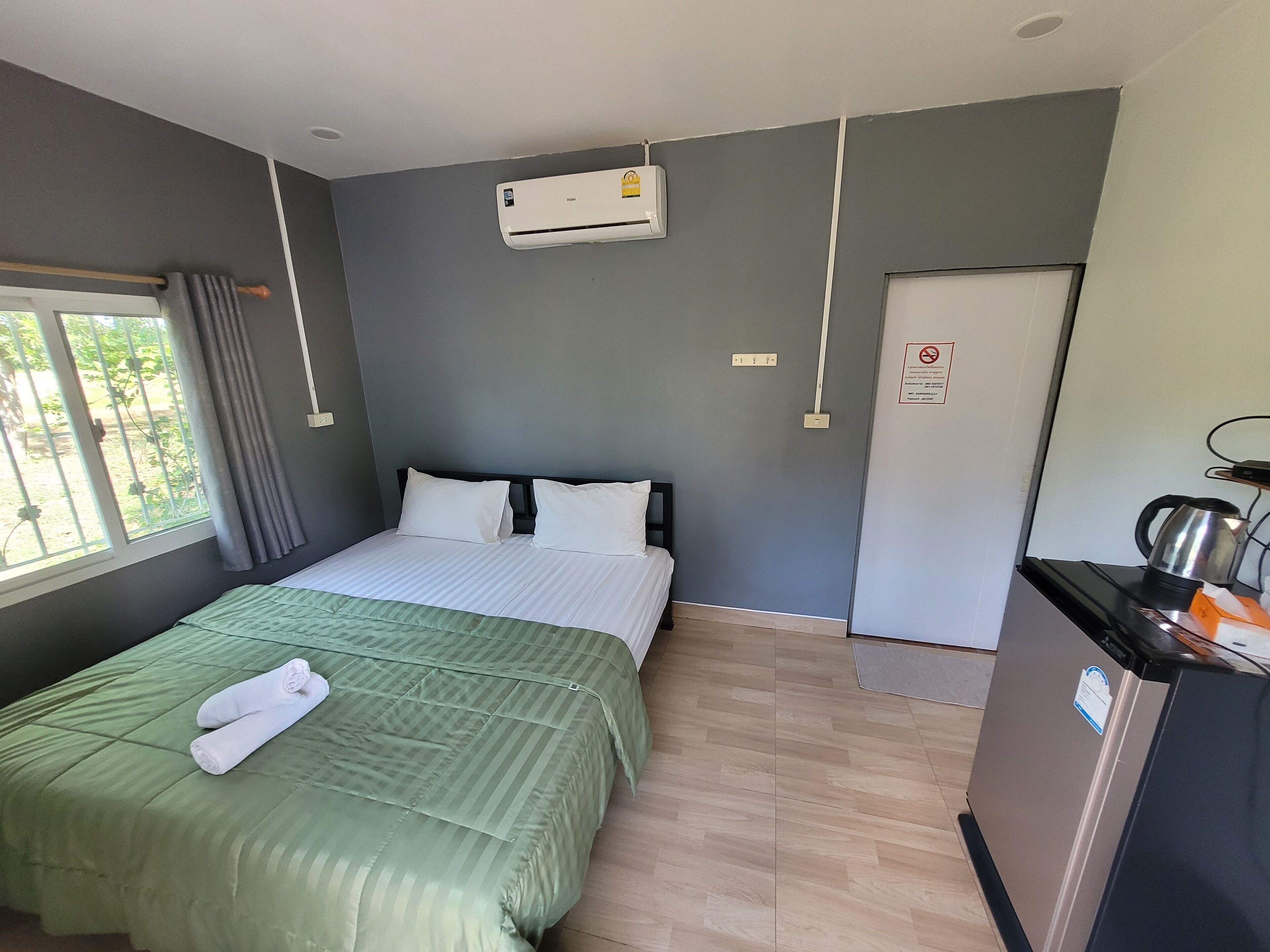Hotelkamer met een bed, een bureau met waterkoker, een airconditioner en een raam met gordijnen.