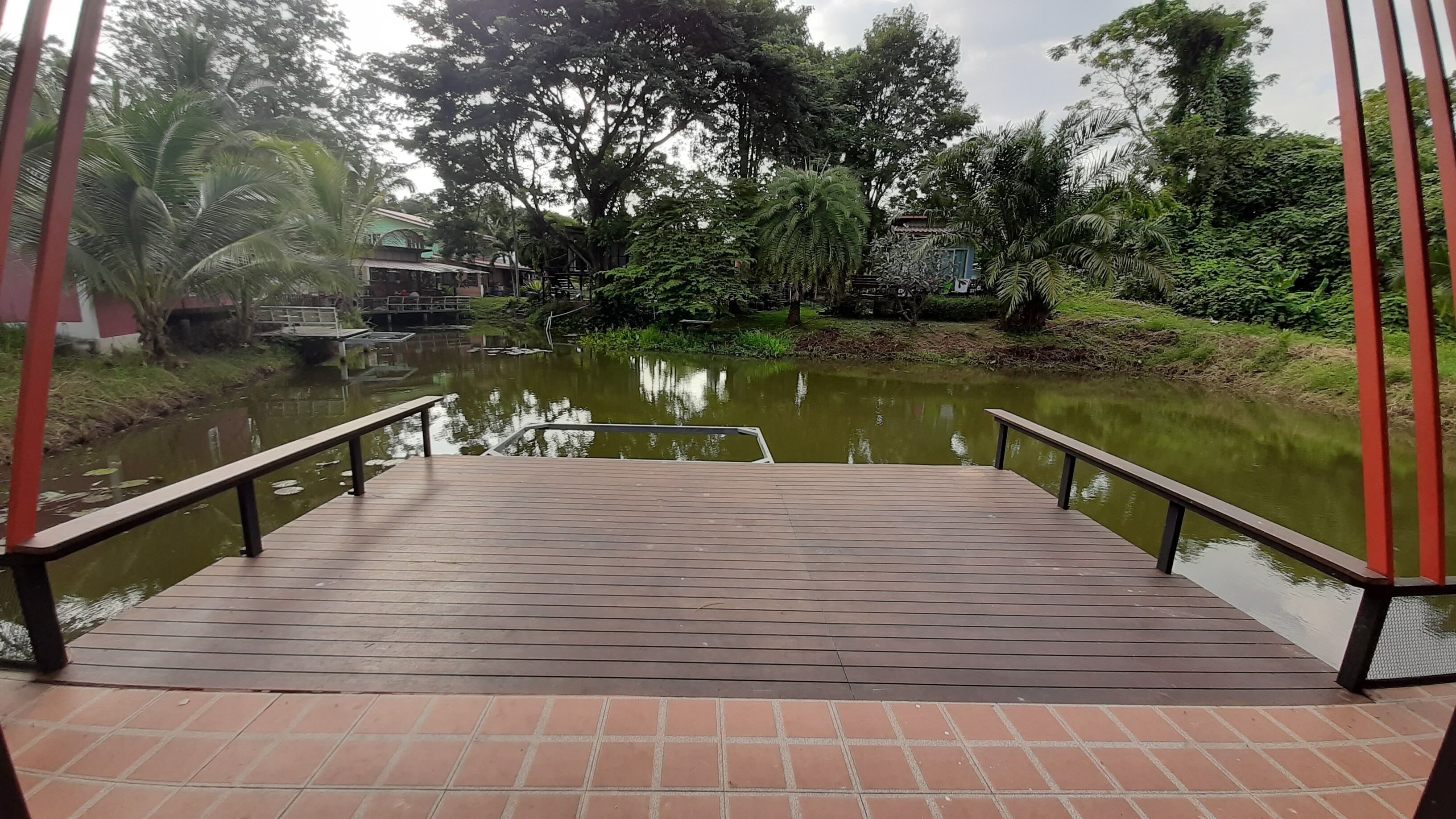 A wooden deck with metal railings overlooking a calm water body, surrounded by lush greenery and trees.