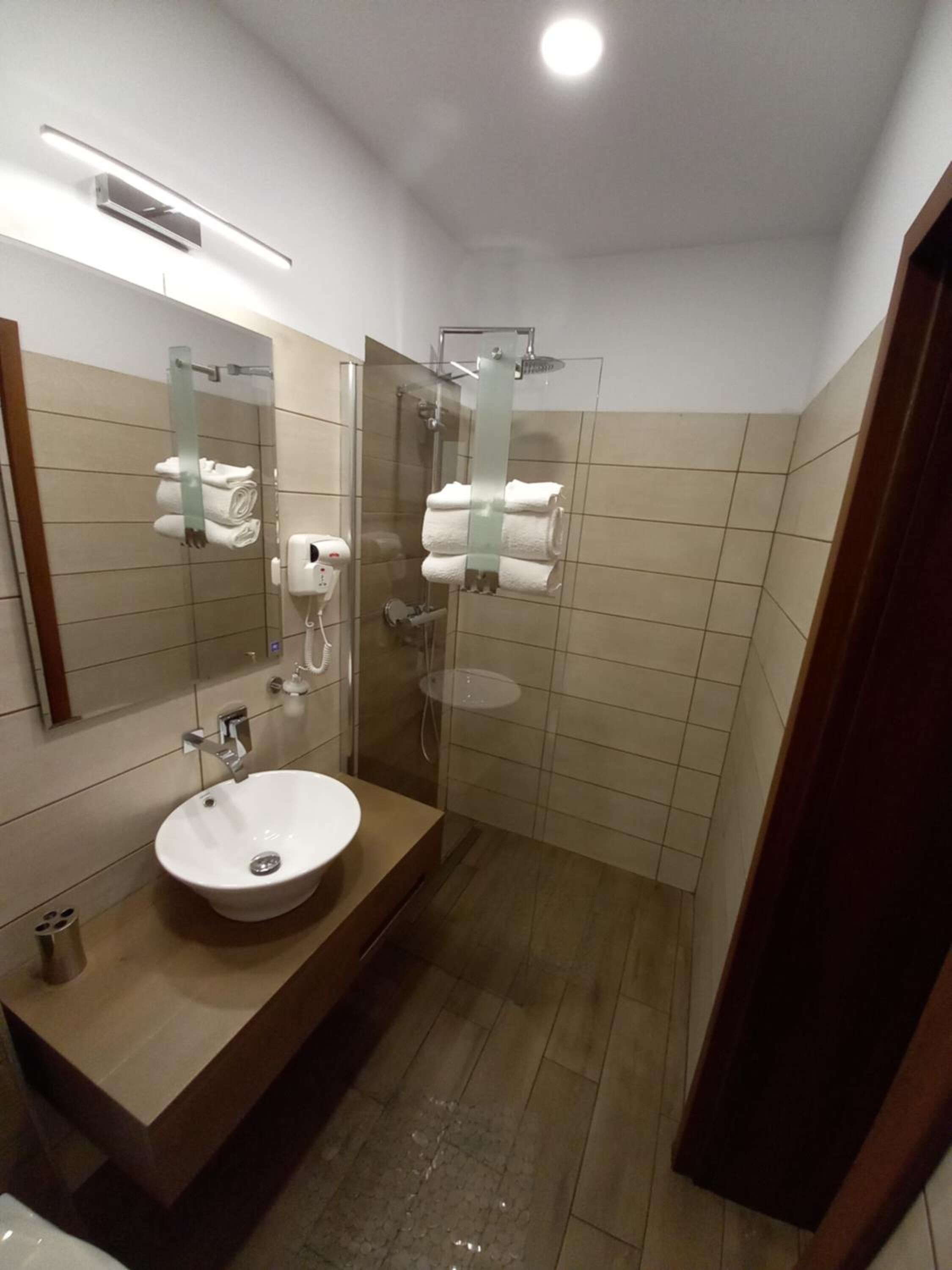 Un baño moderno con lavamanos, espejo, dispensador de toallas y cabina de ducha con mampara de vidrio.