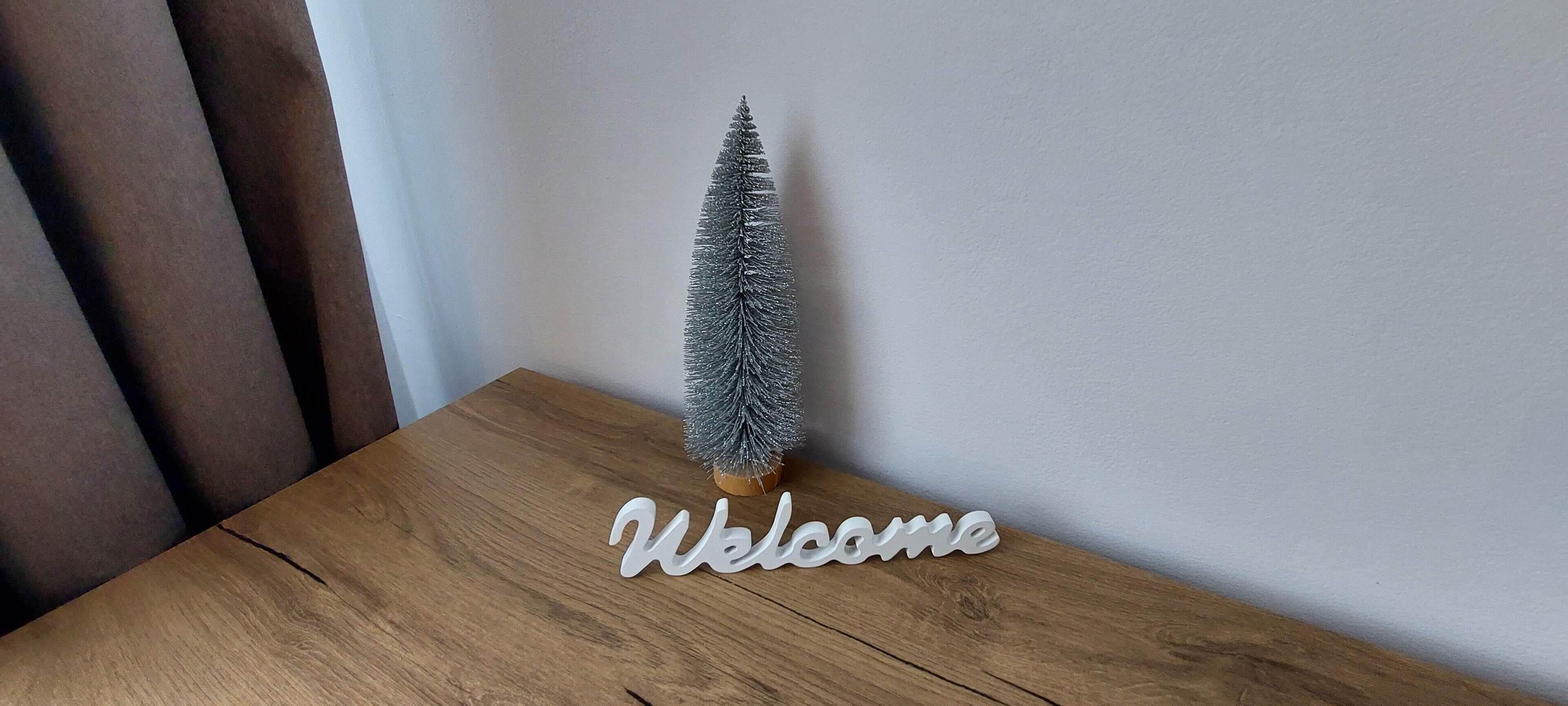 Un pequeño árbol de Navidad plateado sobre una mesa de madera con un letrero que dice 
