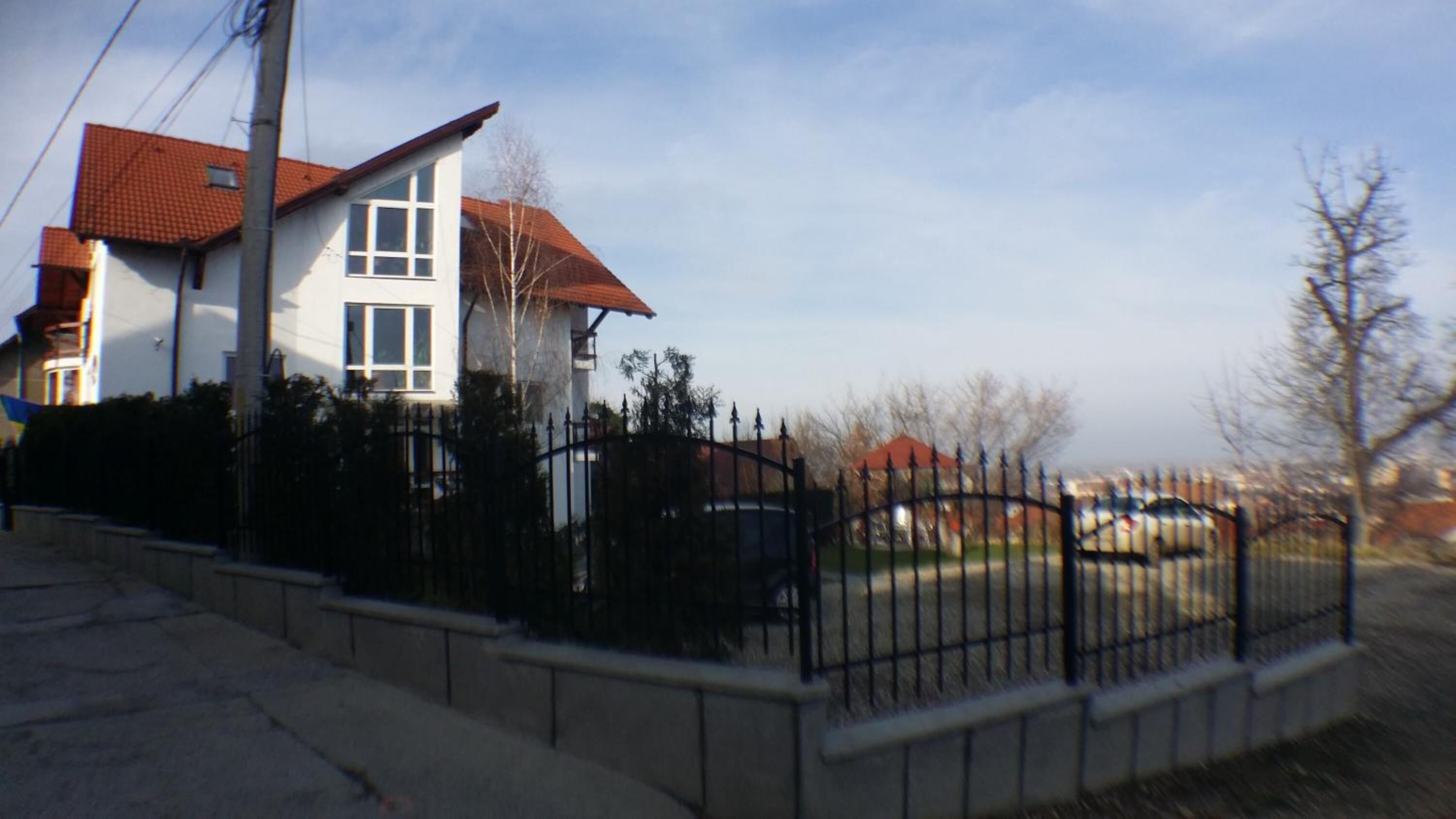 A two-story house with a red-tiled roof, a white exterior, and a black metal fence.