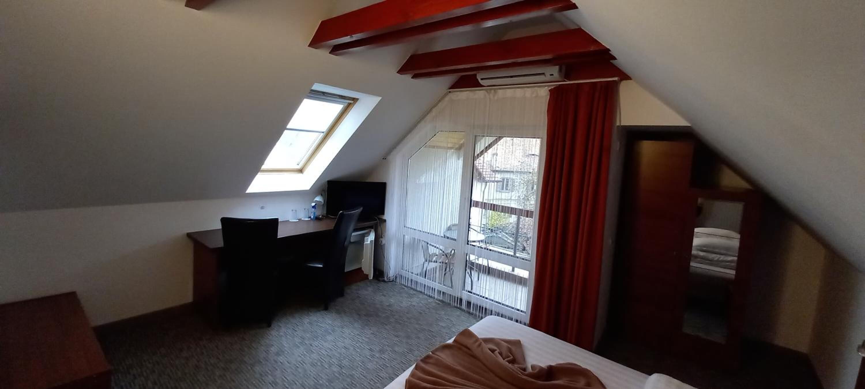 A small, dimly lit room with a sloped ceiling, a desk, a chair, and a bed.